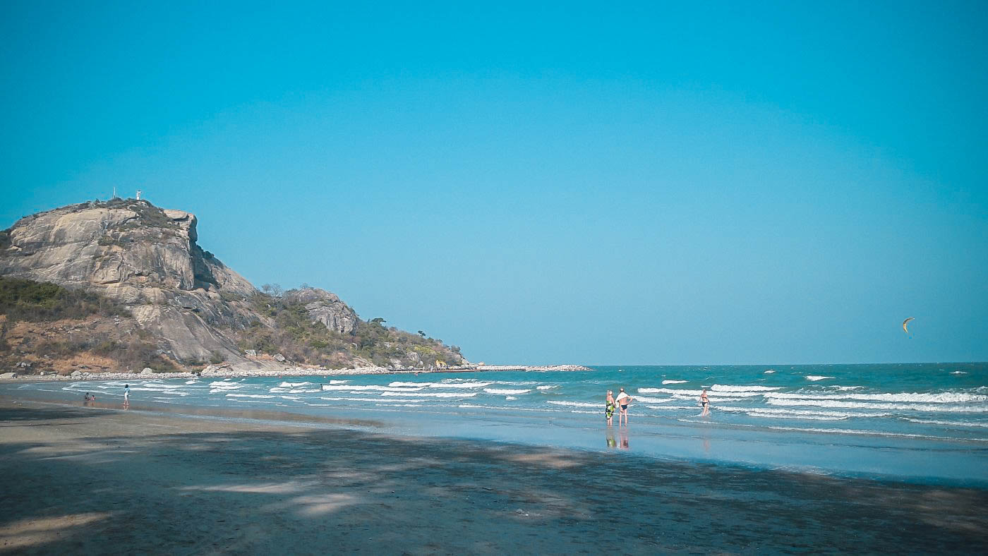 Wet sand reflecting the sky at Khao Takiab with a few people in the shallow water