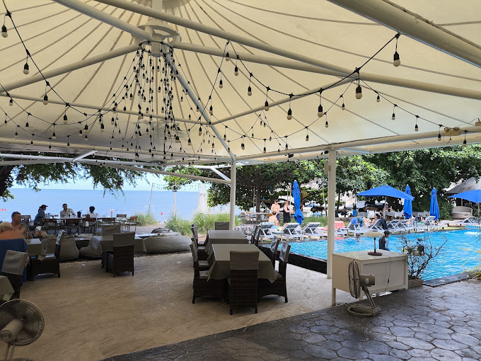 Covered terrace with tables and festoon lighting beside a swimming pool at Kiss Café, Sai Noi Beach