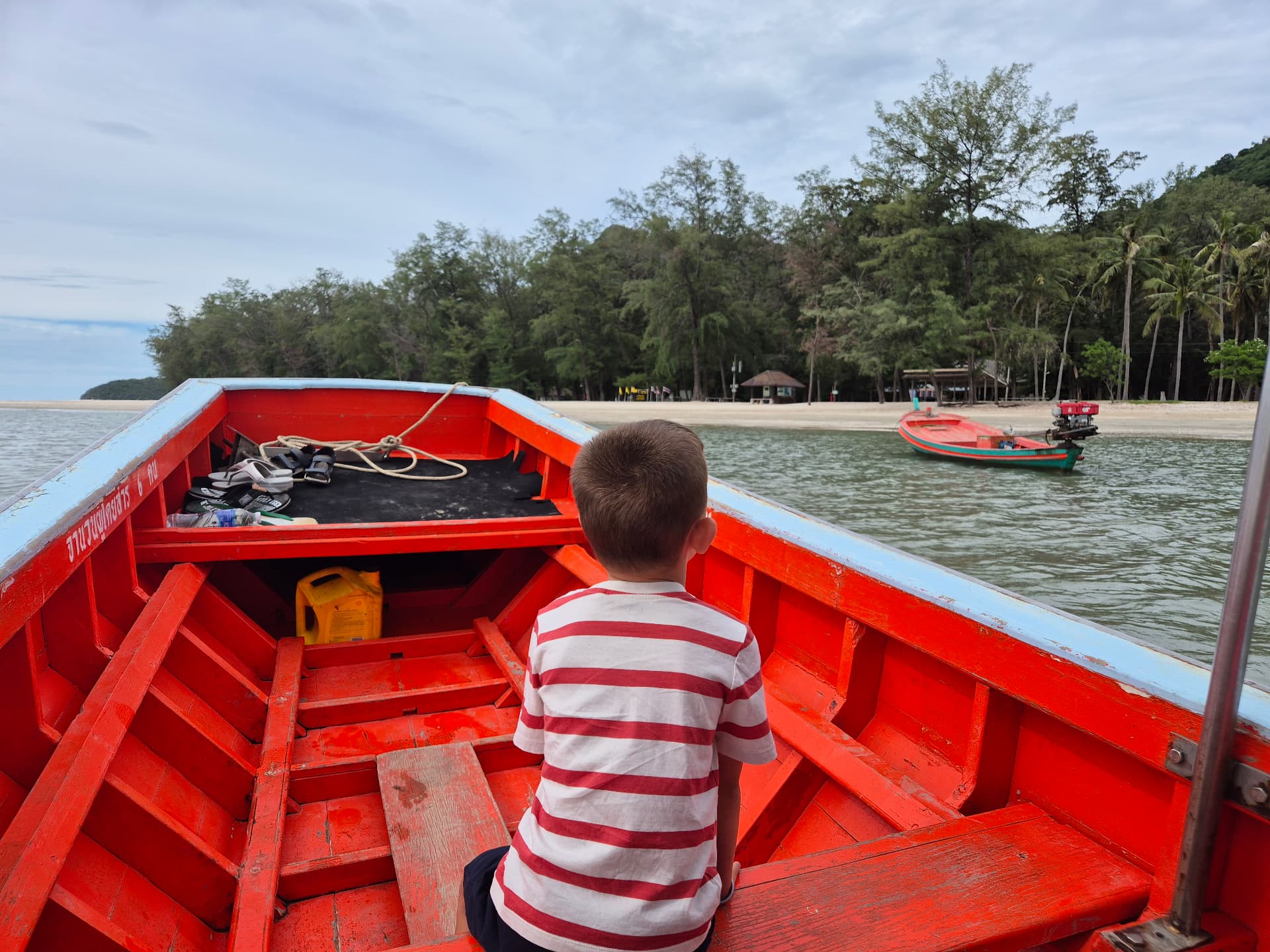 A small red boat approaching a quiet beach backed by forest in Sam Roi Yot National Park
