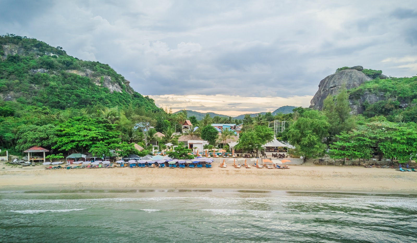 Sai Noi Beach seen from the water, with umbrellas and loungers along the sand below forested hills