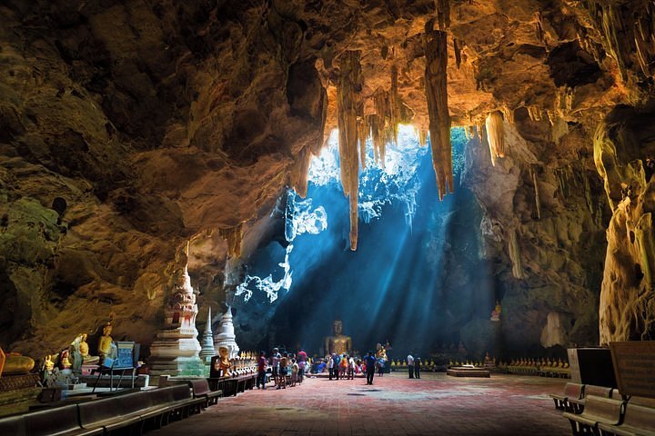 Daylight falling through openings in the roof of Khao Luang Cave onto Buddha images below