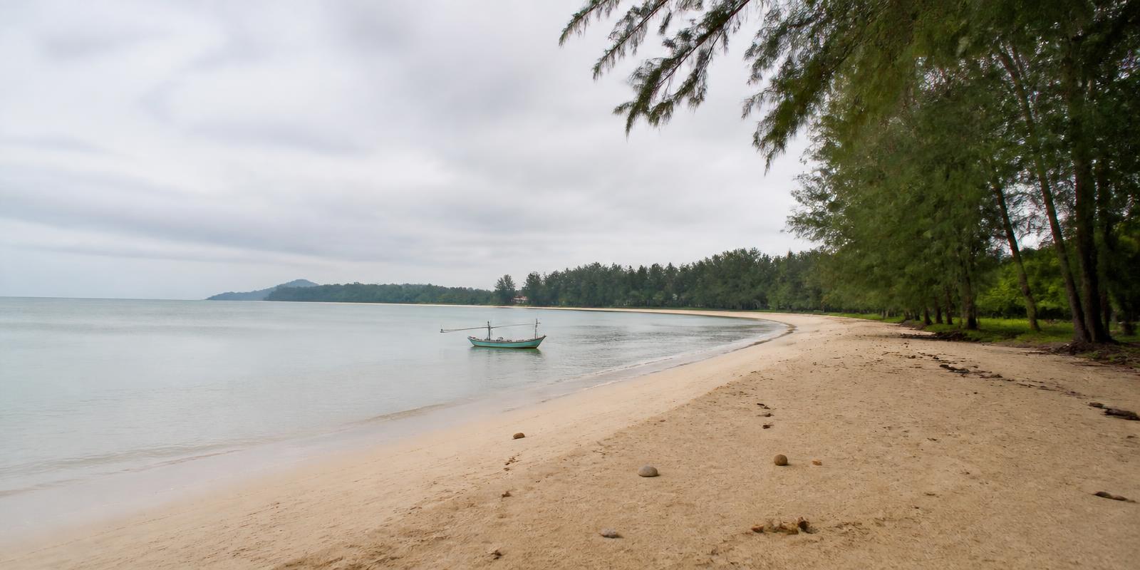 Long quiet beach lined with casuarina pines south of Hua Hin with a small fishing boat offshore
