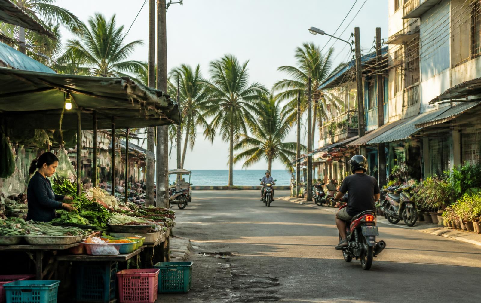 Morning market stall on a quiet street running down to the sea in a Thai coastal town