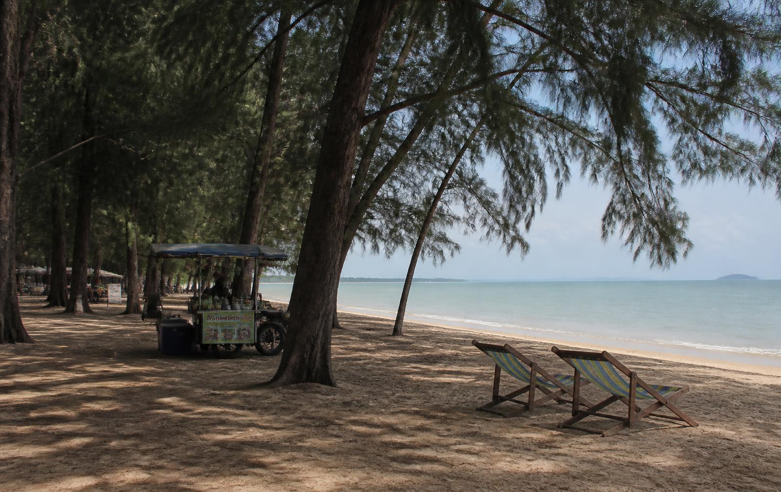 Casuarina pines shading the sand at Suan Son Pradipat beach south of Hua Hin, with deckchairs and a food cart